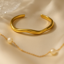 Load image into Gallery viewer, Close-up of Chloe Gold Wave Cuff Bracelet resting on soft satin fabric, minimalist sculptural gold jewelry, modern adjustable open bangle for women.