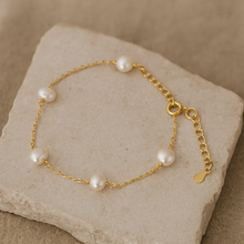 Load image into Gallery viewer, Gold Pearl Chain Bracelet displayed on natural stone plate, featuring five luminous freshwater pearls on a delicate 18K gold plated sterling silver chain, water and tarnish resistant minimalist jewellery by MJ Luxe.