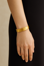 Load image into Gallery viewer, A woman wearing the MJ Luxe Co Colette Gold Textured Cuff Bracelet styled with a black dress. This hammered gold cuff bangle is adjustable, waterproof, tarnish resistant, and crafted in 18K gold plated stainless steel. A versatile piece of minimalist gold jewellery designed for everyday wear, bridal styling, or bridesmaid gifting, perfect for stacking with other bracelets or wearing solo as a statement accessory.