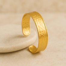 Load image into Gallery viewer, Colette Gold Textured Cuff Bracelet by MJ Luxe Co leaning on a natural stone. This hammered gold open cuff bangle is adjustable, waterproof, tarnish resistant, hypoallergenic, and nickel free. Crafted with premium 18K gold plated stainless steel and PVD plating for durability, this versatile gold bracelet is designed for everyday elegance, stacking, and gifting for bridal parties, anniversaries, or birthdays.