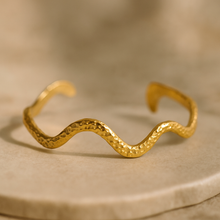 Load image into Gallery viewer, MJ Luxe Hammered Gold Wave Cuff Bracelet displayed on stone surface, textured sculptural bangle with modern wave design.