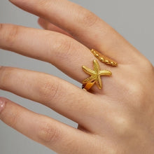 Load image into Gallery viewer, Model wearing the Isla Starfish Seashell Ring on her hand, showing the detailed starfish design in polished gold. The adjustable open ring wraps comfortably, crafted from waterproof stainless steel with 18K gold plating for durability. A chic coastal jewellery piece that adds an elegant ocean inspired touch, making it a perfect everyday ring or thoughtful gift for women.
