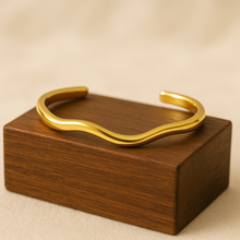 Load image into Gallery viewer, Chloe Gold Wave Cuff Bracelet displayed on wooden block, modern sculptural minimalist jewellery design.

