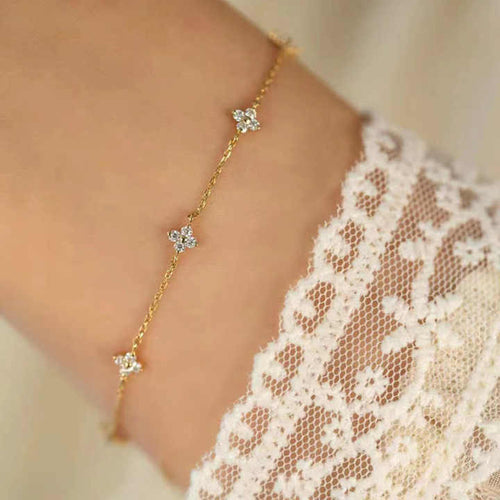 Floral Zircon Gold Bracelet by MJ Luxe worn on the wrist with a lace sleeve. This dainty gold bracelet features sparkling zircon stones in delicate floral motifs, creating an elegant minimalist design. Lightweight and versatile, it is perfect for everyday wear, stacking, or gifting. A timeless piece of jewellery for women, ideal as a bridesmaid gift, bridal accessory, or a thoughtful present for birthdays and anniversaries.