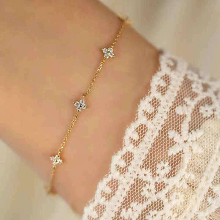 Floral Zircon Gold Bracelet by MJ Luxe worn on the wrist with a lace sleeve. This dainty gold bracelet features sparkling zircon stones in delicate floral motifs, creating an elegant minimalist design. Lightweight and versatile, it is perfect for everyday wear, stacking, or gifting. A timeless piece of jewellery for women, ideal as a bridesmaid gift, bridal accessory, or a thoughtful present for birthdays and anniversaries.