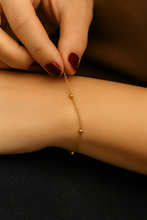 Load image into Gallery viewer, Woman adjusting a delicate gold bead bracelet with polished finish, dainty and stackable minimalist jewellery piece by MJ Luxe.
