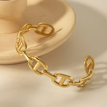 Load image into Gallery viewer, Gold Chain-link Cuff Bracelet by MJ Luxe Co displayed on a beige dish. This open cuff bracelet features bold interlocking chain links in a polished gold finish, offering a modern yet timeless look. Lightweight and adjustable for a comfortable fit, this minimalist bracelet is perfect for daily wear, layering, or gifting. A versatile piece of gold jewellery ideal for women who love stackable bangles, bridal gifts, and elegant accessories.
