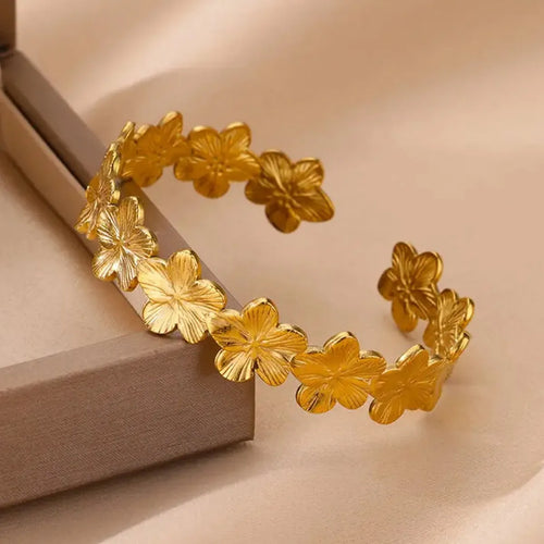 Close-up of an 18K gold plated flower cuff bracelet resting on a neutral jewellery box. The open cuff design features hammered floral petal motifs with a textured finish, crafted from waterproof stainless steel. The gold bangle’s intricate flowers catch the light, making it a versatile statement bracelet for women. Perfect as a floral cuff bangle gift for bridesmaids, anniversaries, or everyday jewellery styling.