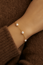 Load image into Gallery viewer, Gold Pearl Chain Bracelet worn on wrist with brown knitwear, dainty freshwater pearl bracelet for women, minimalist gold chain jewellery, timeless everyday piece by MJ Luxe.
