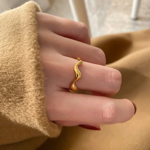Minimalist Gold Wave Ring size 6 in 18K gold plating worn on model’s finger with cosy knit jumper sleeve, showcasing polished wavy silhouette for everyday wear.