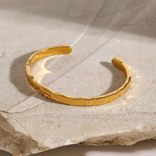 Load image into Gallery viewer, Minimalist hammered gold cuff bracelet photographed flat on stone surface, adjustable open-ended bangle with 18K gold plating, waterproof and tarnish-resistant jewellery.
