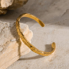 Load image into Gallery viewer, Aurora Hammered Gold Cuff Bracelet angled on textured stone, featuring hammered finish and modern open cuff design, luxury gold bangle ideal for stacking or solo wear.
